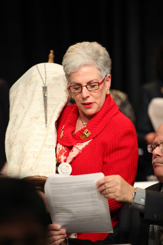 Helene Waranch in a red blazer holding a Torah