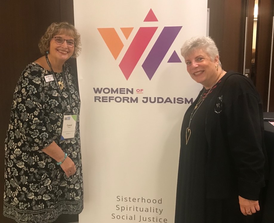 Two women stand in front of a banner featuring Women of Reform Judaism. 