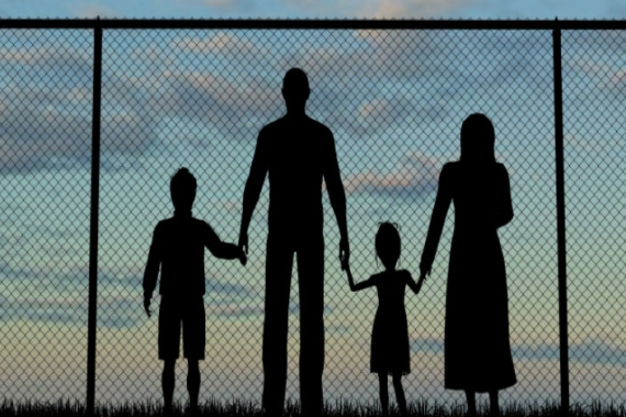 Silhouette of family members holding hands in front of a chain link fence