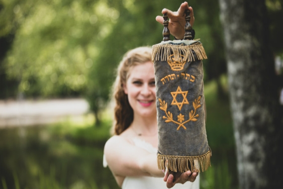 Smiling teenage girl in the background holding a small Torah to the camera