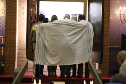 an image of four people standing in front of an open arch with a tallit spread out across their backs
